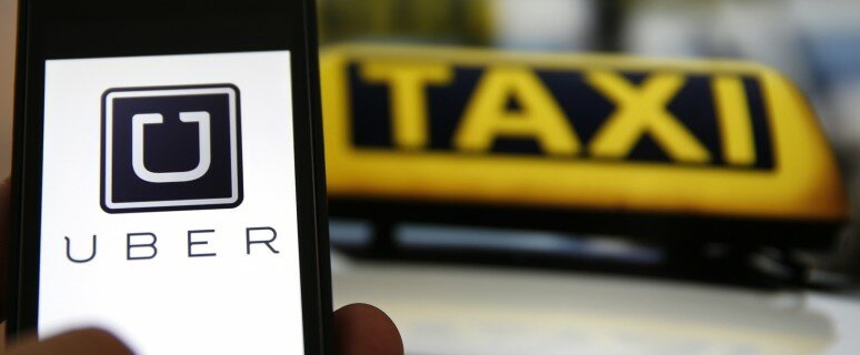 File illustration picture showing the logo of car-sharing service app Uber on a smartphone next to the picture of an official German taxi sign